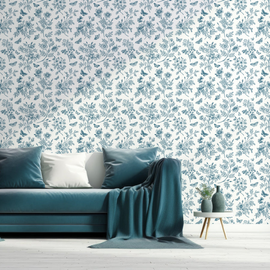 A living room with a blue velvet sofa featuring the Alice wallpaper which is a white wallpaper with vintage blue roses, delicate butterflies and leafy stems in an elegant repeating floral pattern.