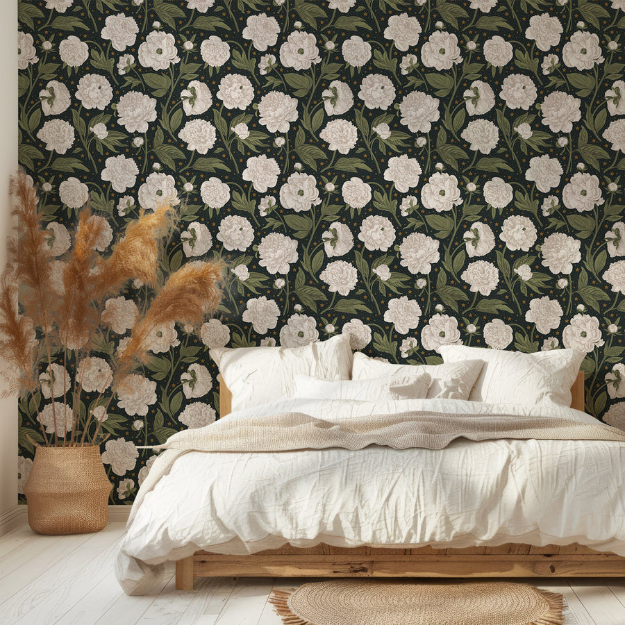 An urban bedroom with white bedding and a rattan basket with pampas grass in it, showing 'Celestial' which is a dark green botanical wallpaper featuring large white peony flowers, delicate green leaves and golden star details in a vintage-inspired repeating floral pattern.