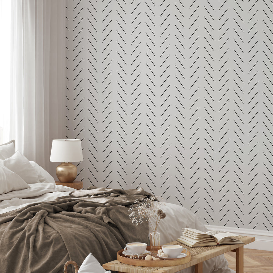 A relaxed styled bedroom showing the Livia wallpaper which is a monochrome wallpaper featuring a minimalist herringbone pattern made from thin diagonal lines arranged in a repeating geometric design.
