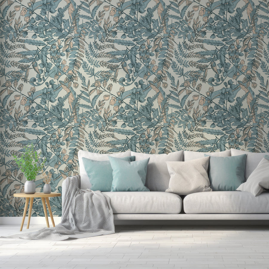 A living room with a light coloured sofa with pillows and a side table with plants featuring 'Maisie' which is a botanical wallpaper featuring blue and cream illustrated leaves on a soft sage green background in a vintage-inspired repeating foliage pattern.