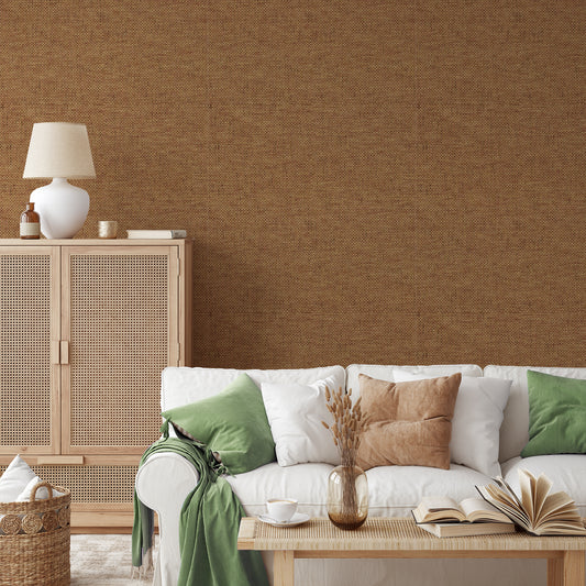 A living room with rattan style furniture showing 'Olive' which is a brown wallpaper featuring a subtle grass cloth texture with woven fibres and natural tonal variations in a repeating textured pattern.
