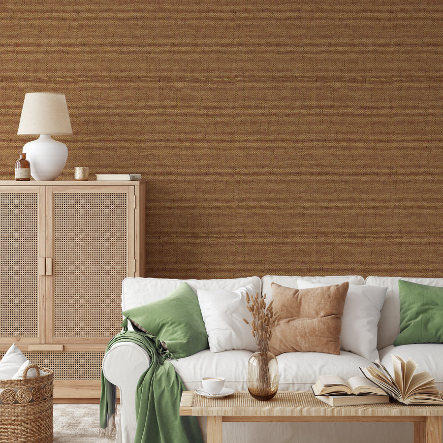 A living room with rattan style furniture showing 'Olive' which is a brown wallpaper featuring a subtle grass cloth texture with woven fibres and natural tonal variations in a repeating textured pattern.