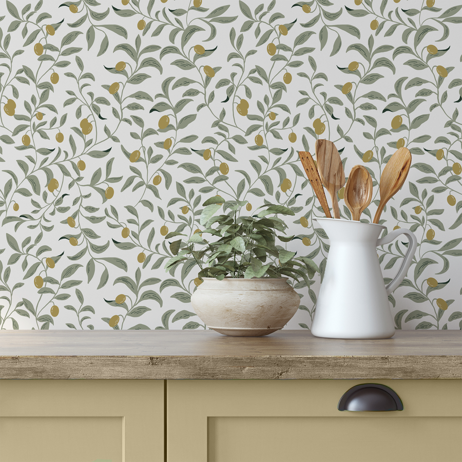 A kitchen worktop with cooking utensils on top next to a green leafy plant featuring 'Olea' which is a mediterranean botanical wallpaper featuring delicate olive tree branches with green leaves and small olives on a soft neutral background in an elegant repeating pattern.