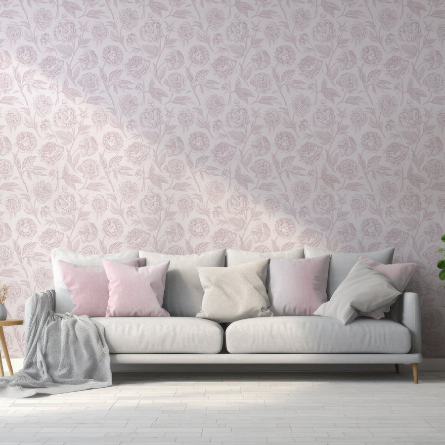 A living room showing a sofa with pillows across it featuring the Paisley wallpaper which is a light pink wallpaper featuring vintage-style dark pink peonies and leafy botanical details in a repeating floral pattern.
