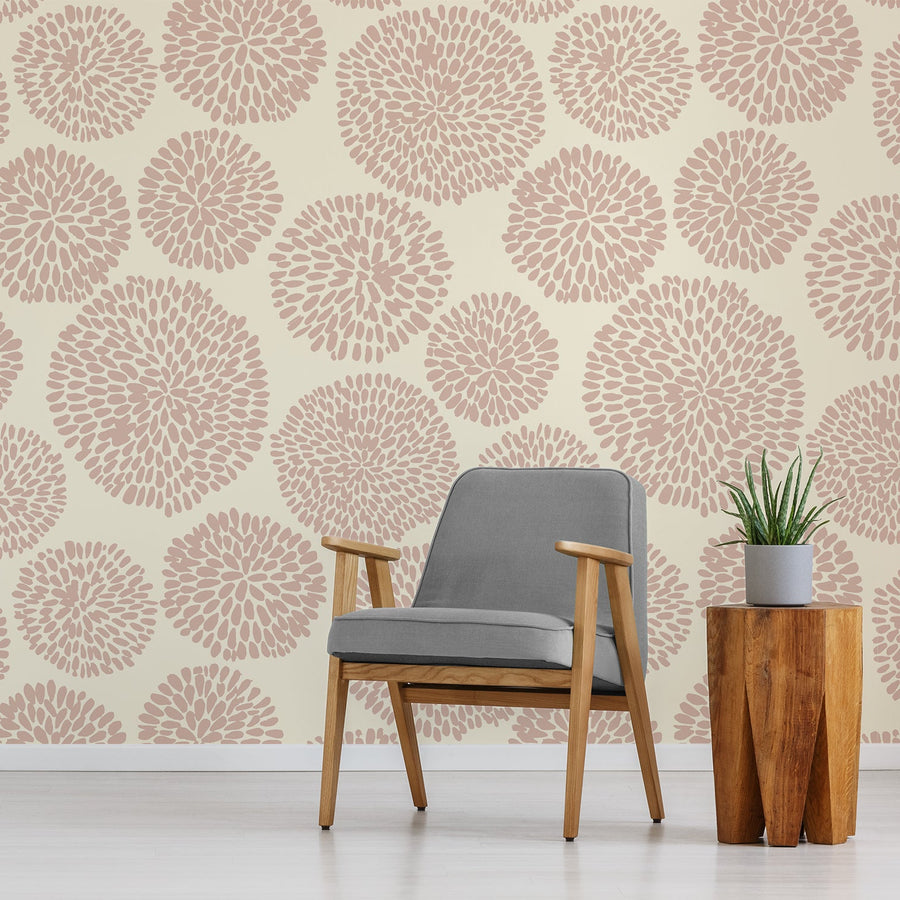 A living room with a single sitting chair next to a potted plant on an amber wood side table featuring the wallpaper Auxence Taupe which is taupe and cream colours with an abstract repeating pattern of segmented circles in soft neutral tones.