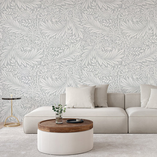 A room with a light coloured sofa with a low coffee table showing 'Beatrix' which is a botanical wallpaper featuring realistic green leaves, twigs and branches arranged in a natural repeating pattern on a light background.
