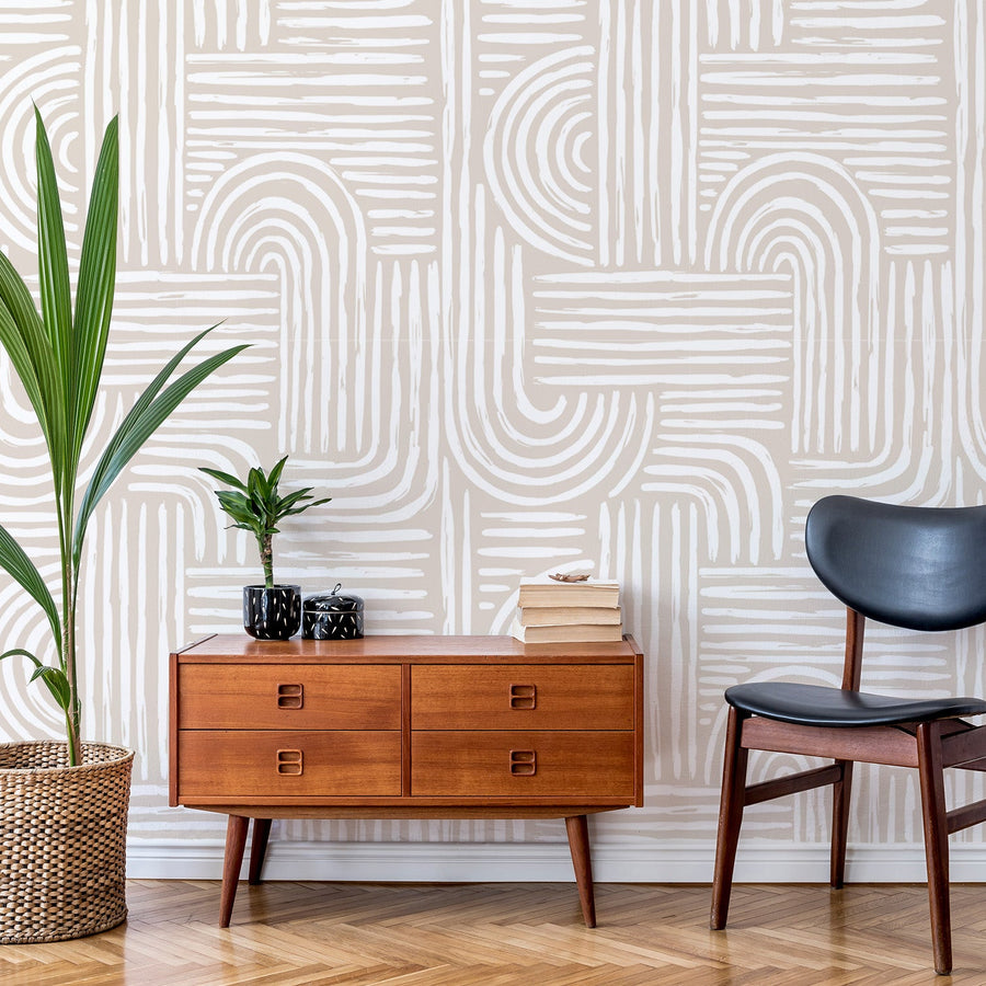 A sitting area with a black leather chair, a low level side table in amber wood and a large leafy plant showing 'Constance' which is an abstract wallpaper featuring layered paint brush strokes in soft beige and white tones, creating a modern textured artistic pattern.